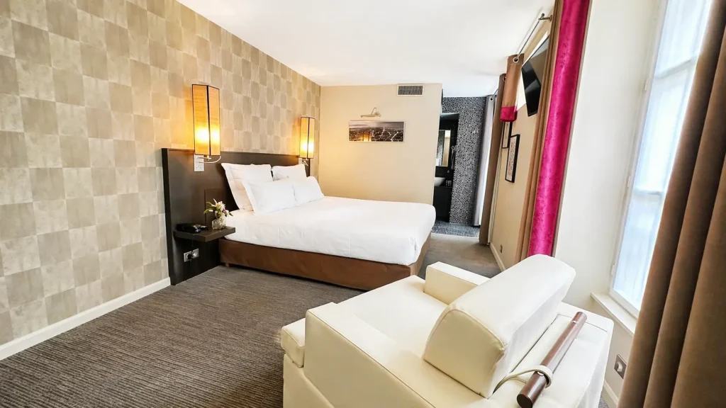 Chambre triple deluxe de l'Hotel Aero Paris avec fauteuil creme et apercu de la salle de bain en mosaique noire